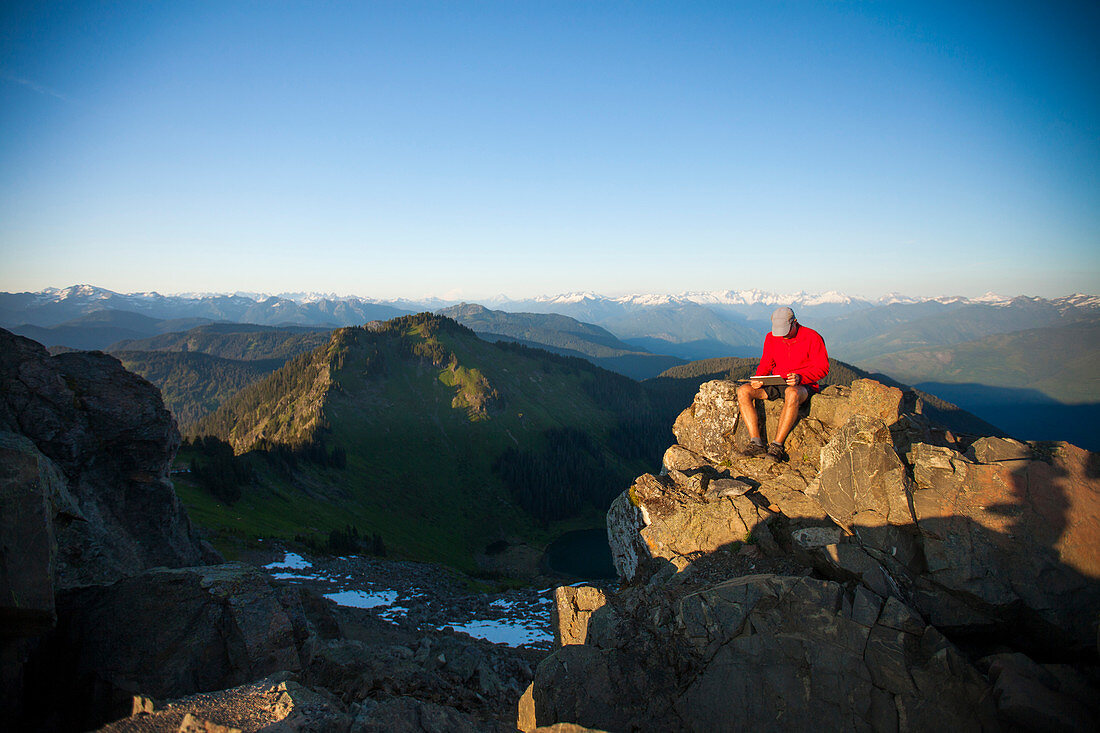A man works on a tablet while sitting on the summit of Sauk Mountain, Washington.