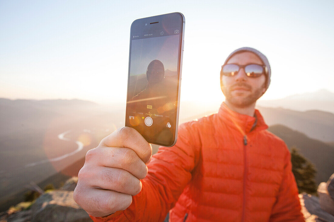A man uses his smartphone to take a selfie while enjoying the outdoors just before sunset.