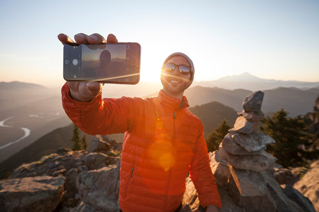 A man uses his smartphone to take a selfie at sunset from the summit of Sauk Mountain, Washington.
