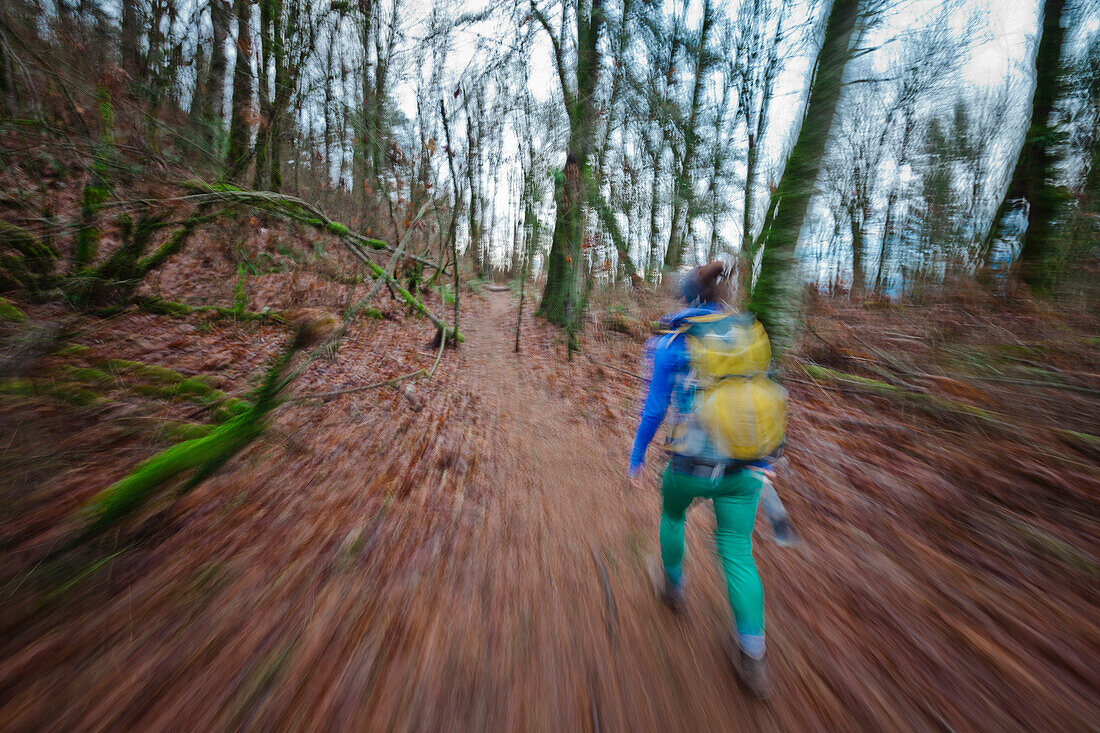 Blurred motion of a young active woman hiking through a dense forest
