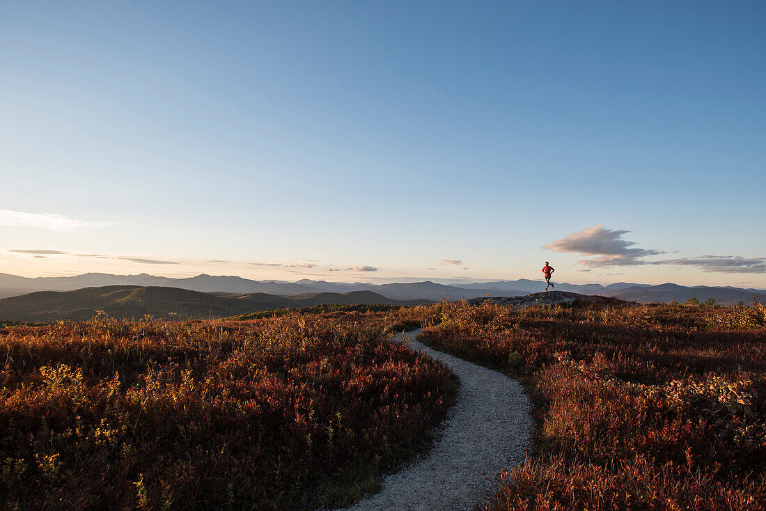 The small shape of a runner near the top of Foss Mountain, with Mt. Washington and the presidential range of the WHite Mountains in the skyline.