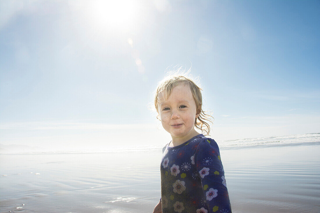 Portrait of happy toddler girl with sun flare on Cannon Beach, Oregon.