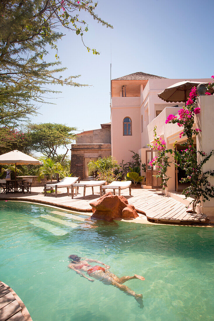 A young woman swims underwater in a small resort's light green pool.