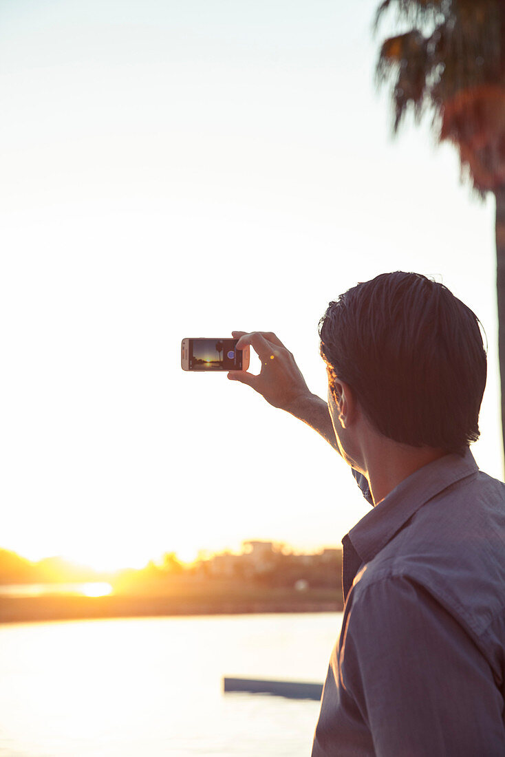 Man photographing sunset with smartphone