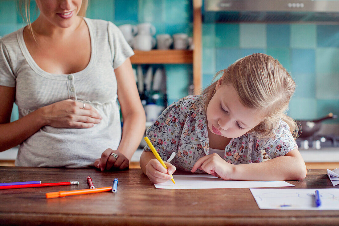 Pregnant mother looking on as daughter draws