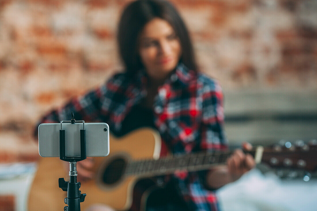 Smart phone in monopod with woman playing guitar in background at home