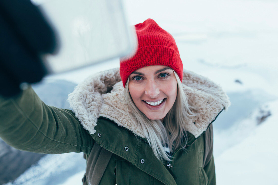 Lächelnde junge Frau, die im Winter ein Selfie mit ihrem Smartphone macht