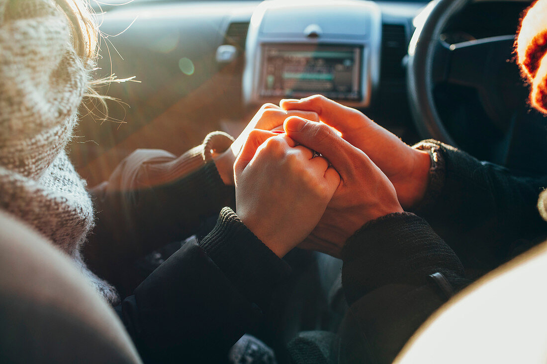 Cropped image of couple holding hands in car