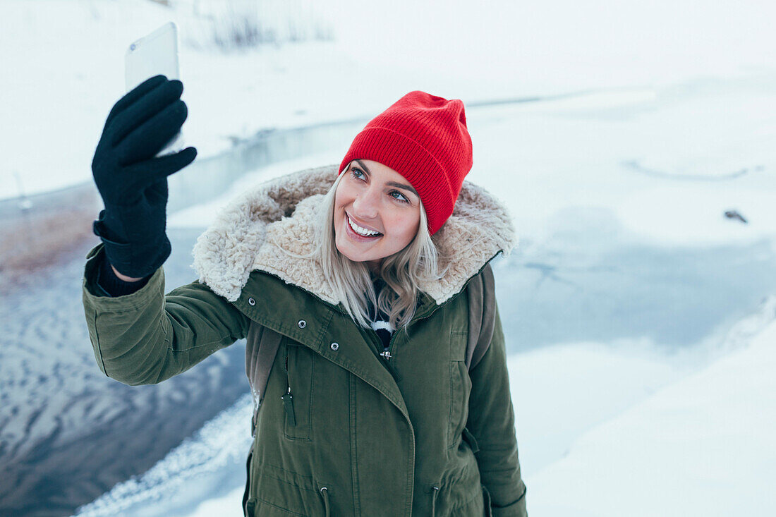 Happy young woman taking selfie on smart phone during winter