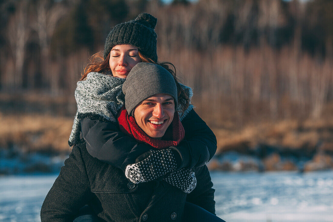 Portrait of happy man giving piggyback ride to woman during winter