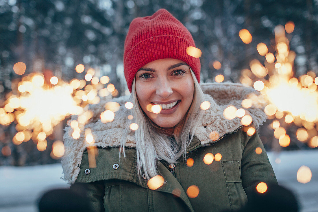 Portrait of smiling woman holding sparklers during winter
