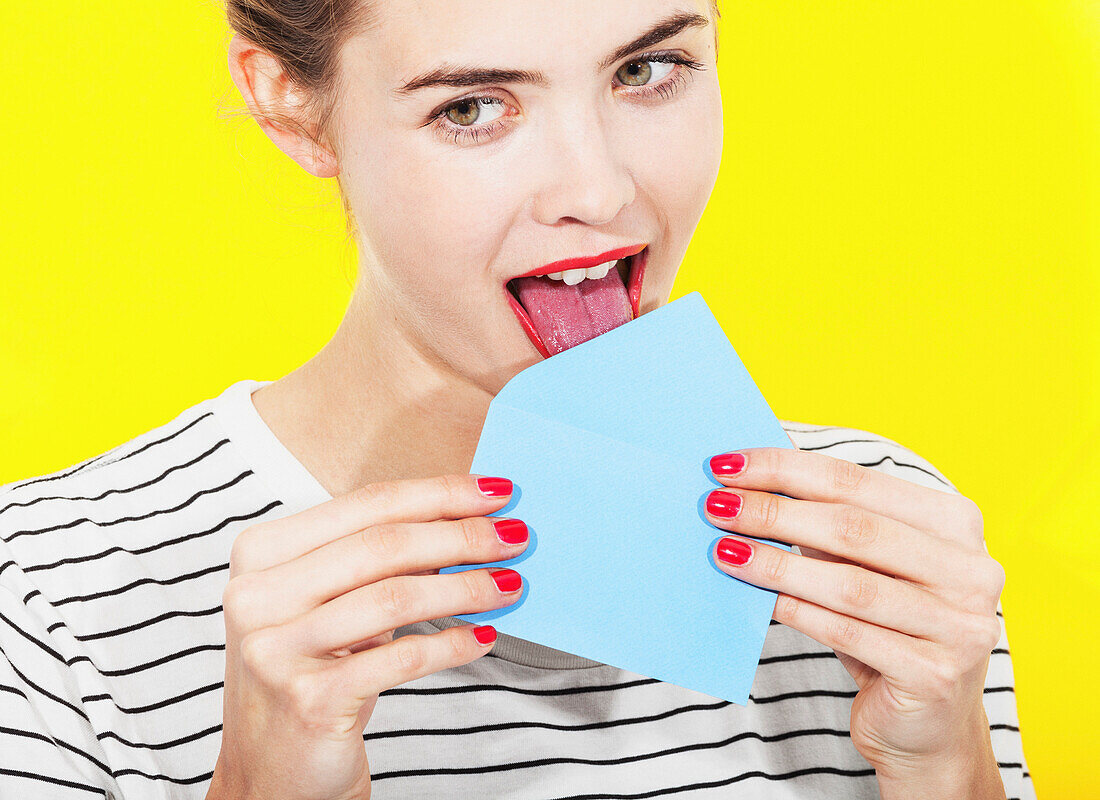 Beautiful woman licking blue envelope against yellow background