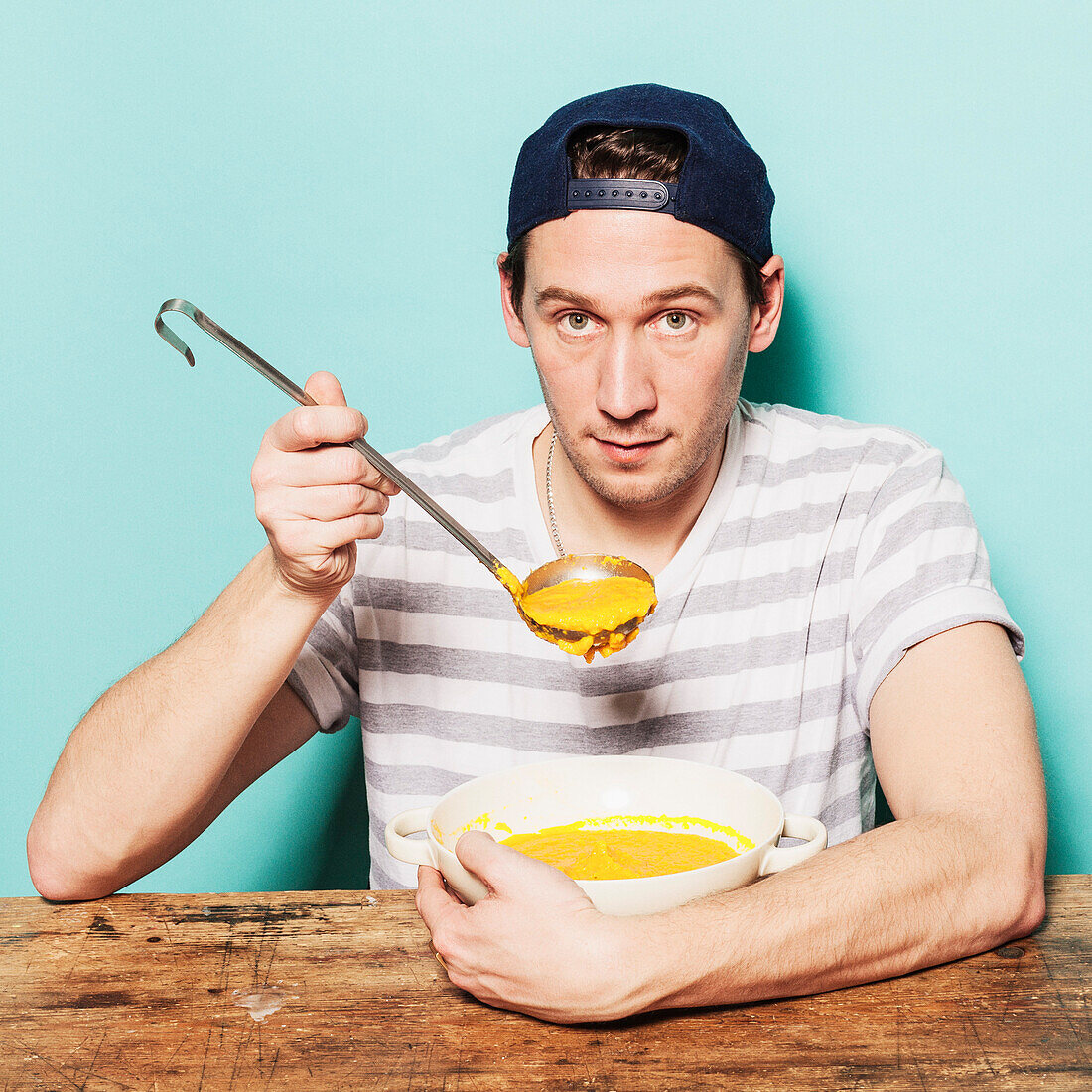 Portrait of confident man having pumpkin soup at table against blue background