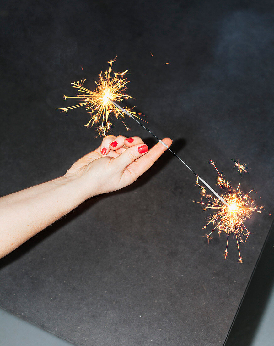 Cropped image of woman balancing sparklers on fingers