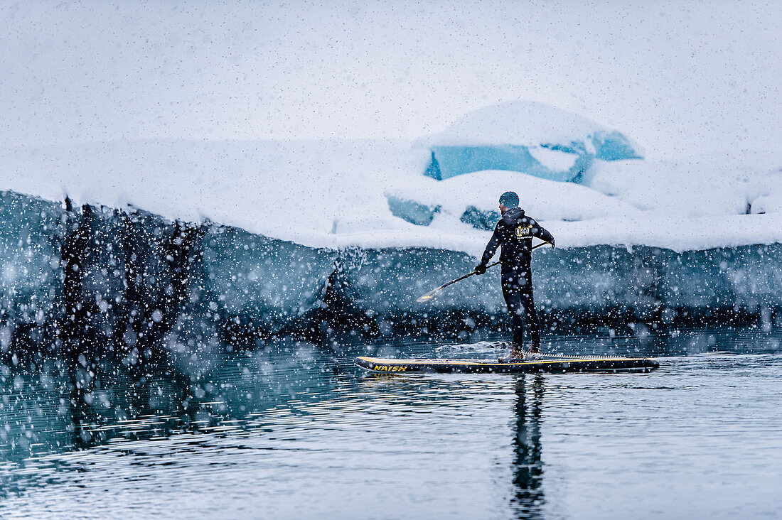 Man stand up paddling on a glacier lagoon Jokulsarlon at Vatnajokul, Iceland