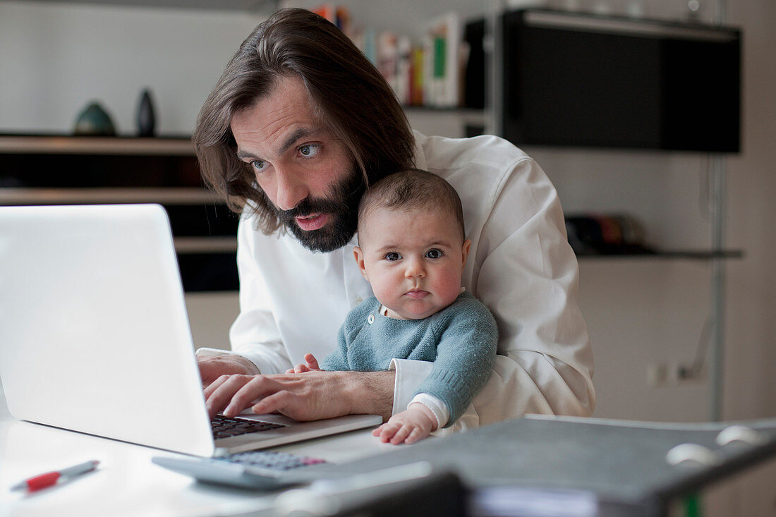 Man working on laptop while sitting with baby girl at home