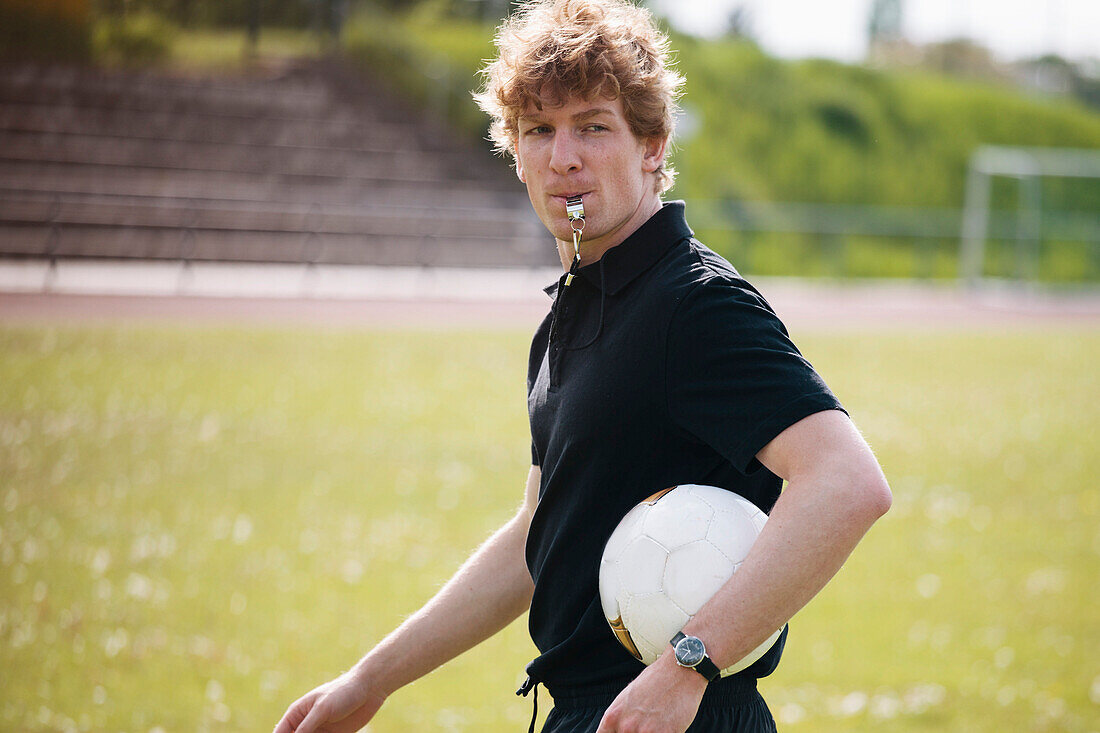 Referee blowing whistle while carrying soccer ball on field