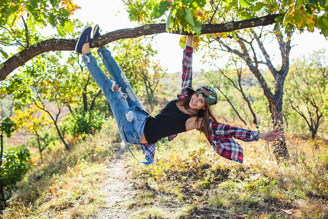 Full length of happy young woman climbing from branch in forest