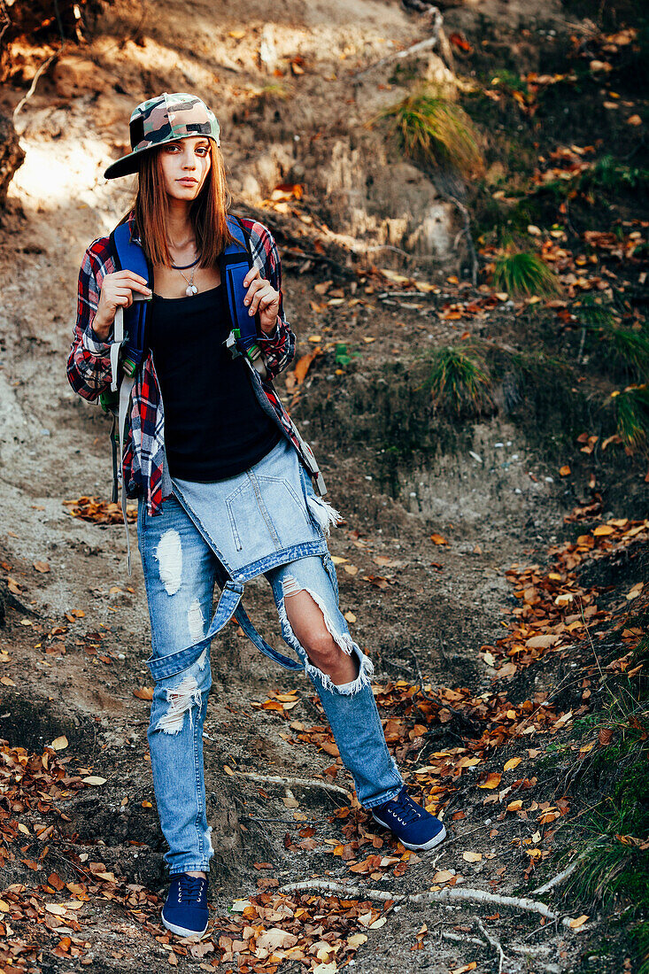 Full length portrait of fashionable young woman wearing torn jeans in forest