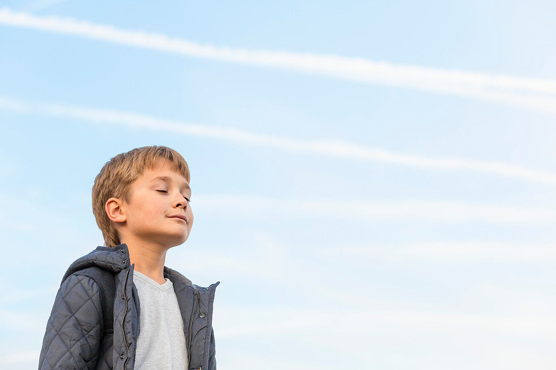 Low angle view of boy with eyes closed against sky