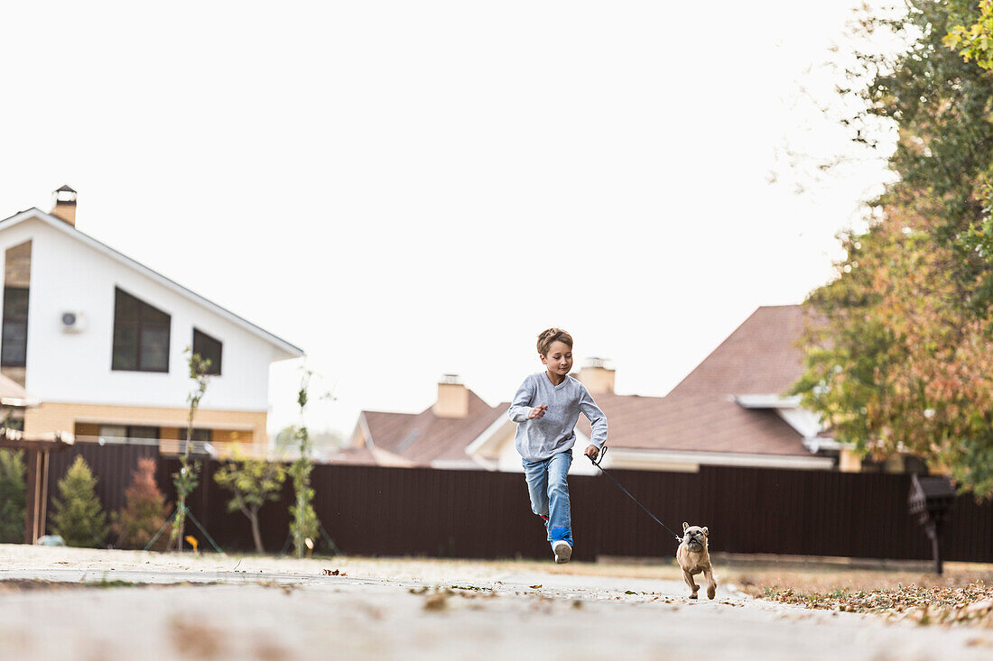 Boy running with dog on footpath against clear sky
