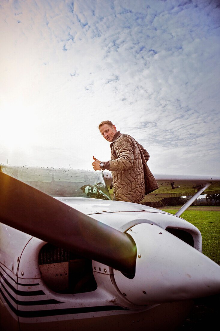Side view portrait of man gesturing thumbs up by private airplane against sky