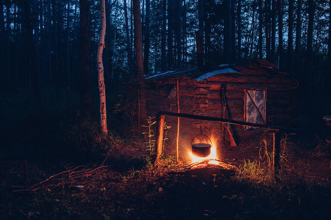 Container hanging over campfire in forest