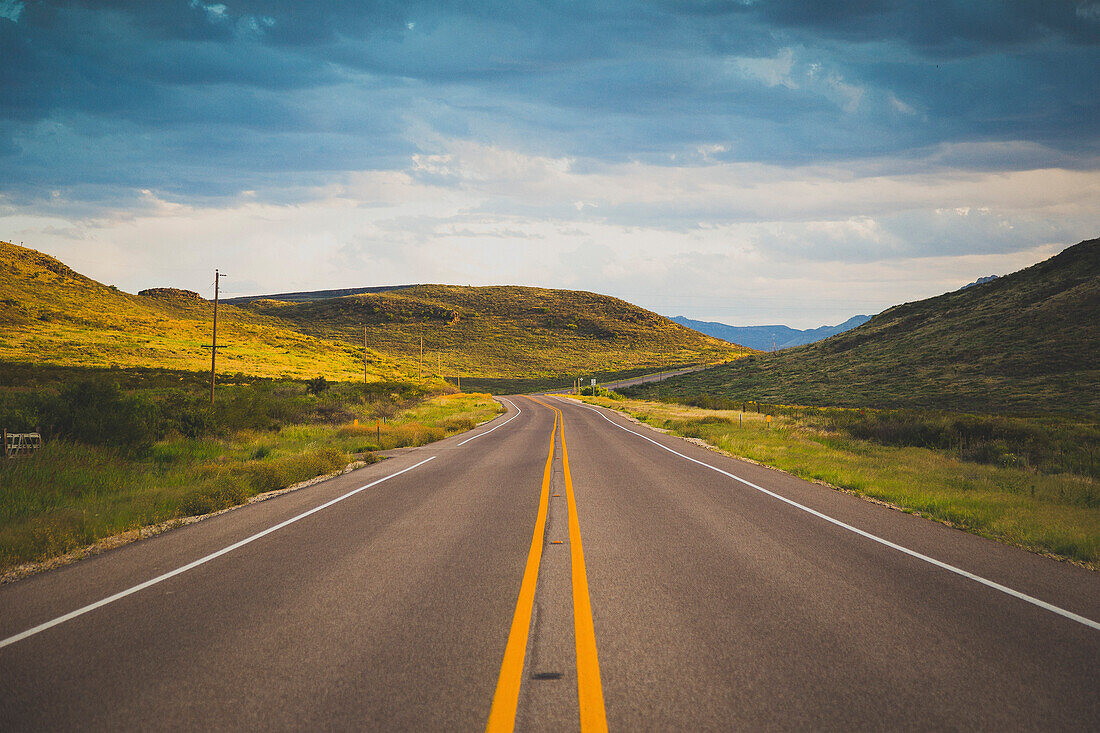 Road leading towards green mountains against cloudy sky