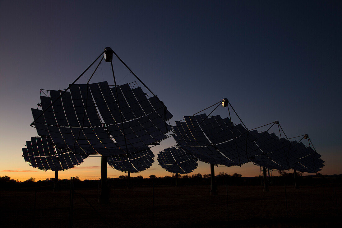 Solar dishes at power station against sky during sunset