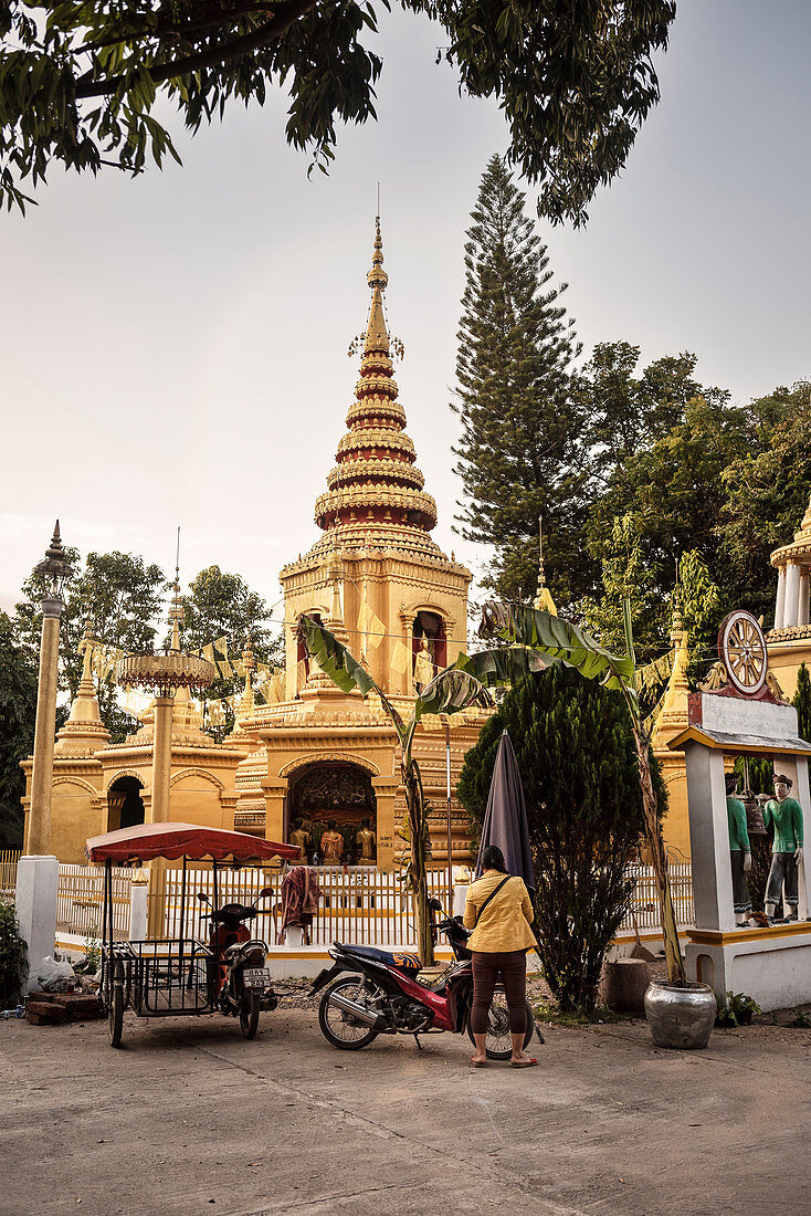 Thailänderin mit gelber Jacke und Motorrad vor goldener Pagode an einem Tempel in Pai, Thailand, Südost Asien