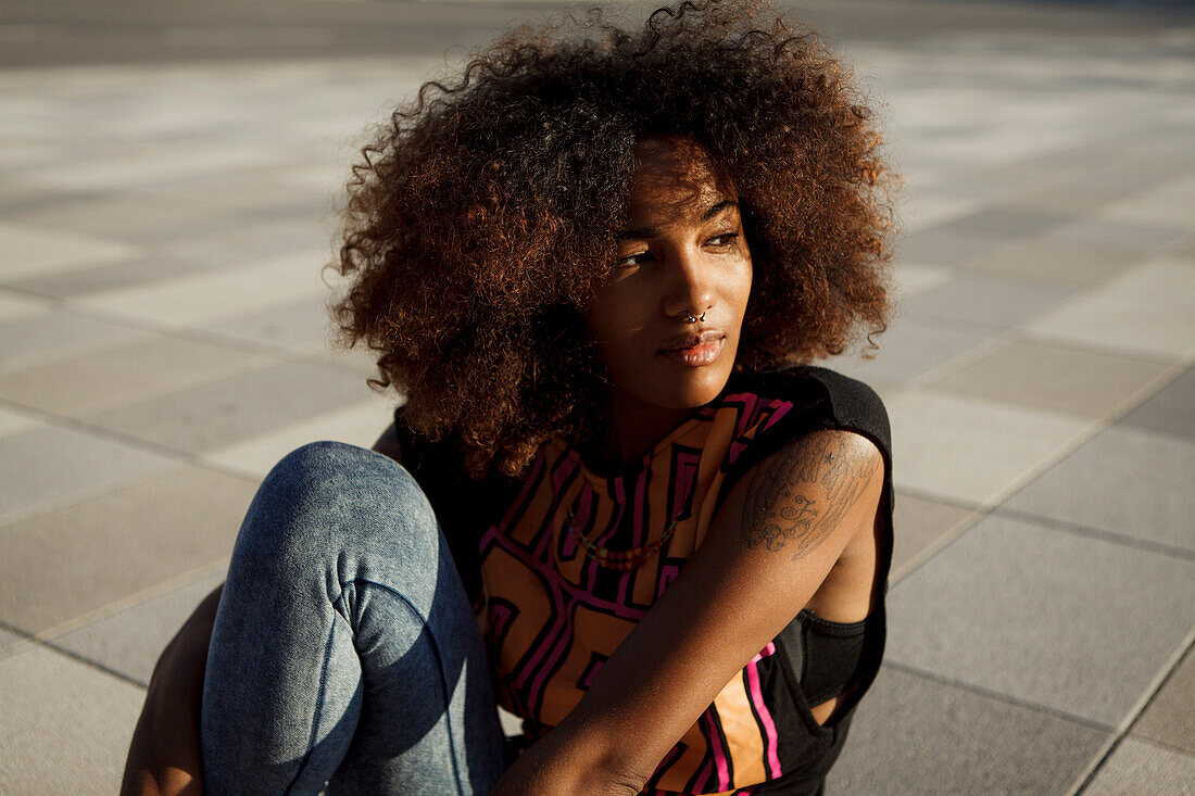 Sportliche junge afroamerikanische Frau sitzt cool auf grafischem Boden, Lenbachplatz, München, Bayern, Deutschland