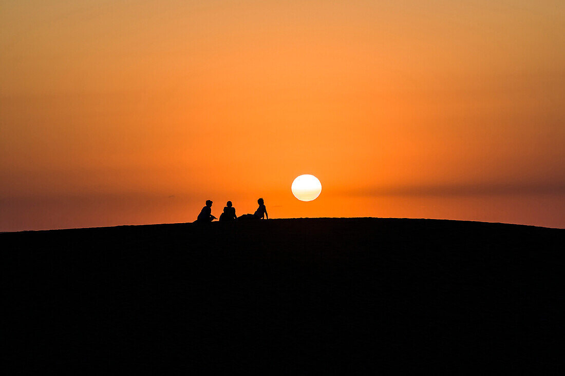 A group during sunset as a silhouette in front of the sun ball on the largest sand dune of the East coast, Nags Head, Outer Banks, North Carolina, USA