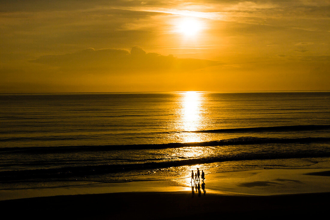 4 Personen als Silhouette gehen am Strand bei Sonnenaufgang am Atlantik spazieren, Daytona Beach, Florida, USA