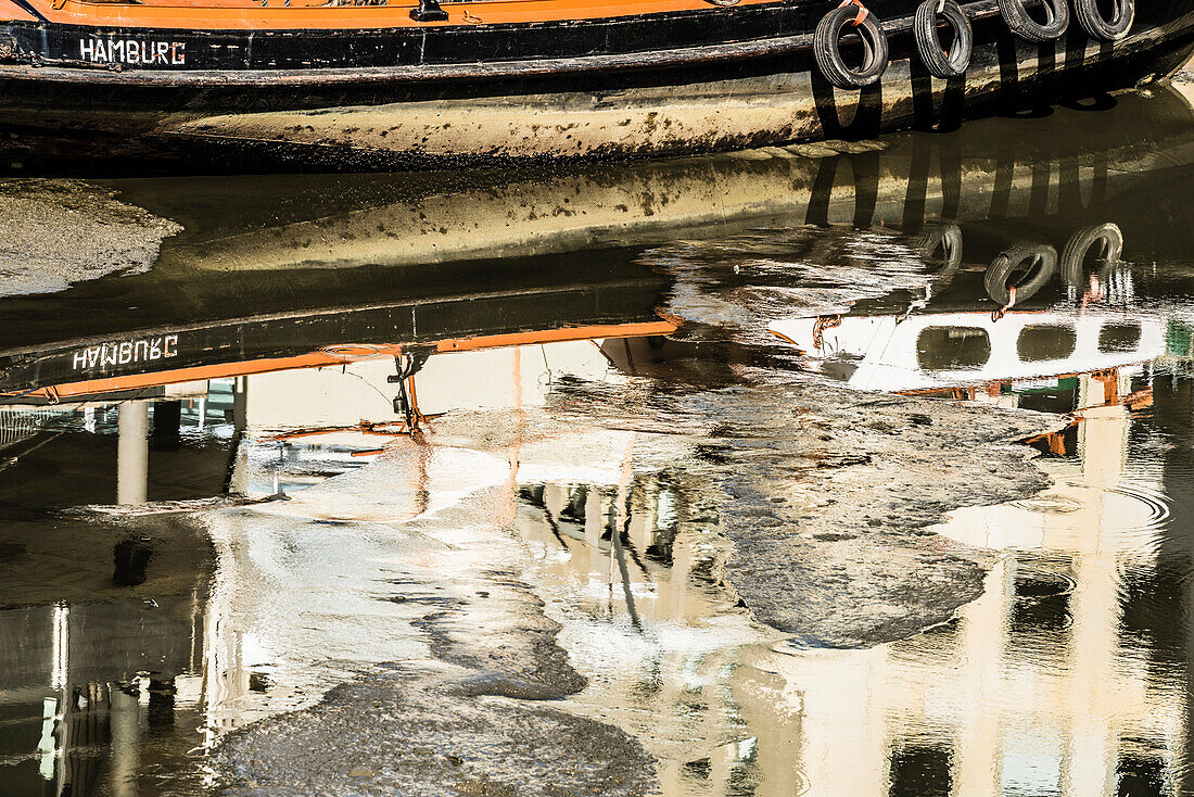 A small cargo vessel with Hamburg sign which is reflected in the water in the almost dry-fallen canal, Hamburg, Germany