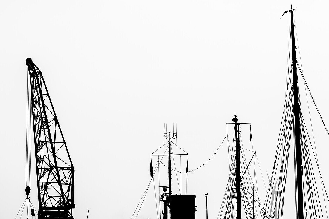 Silhouette einer Spitze eines alten Kranes und die Takelage von alten Schiffen im Museumshafen Oevelgönne, Hamburg, Deutschland