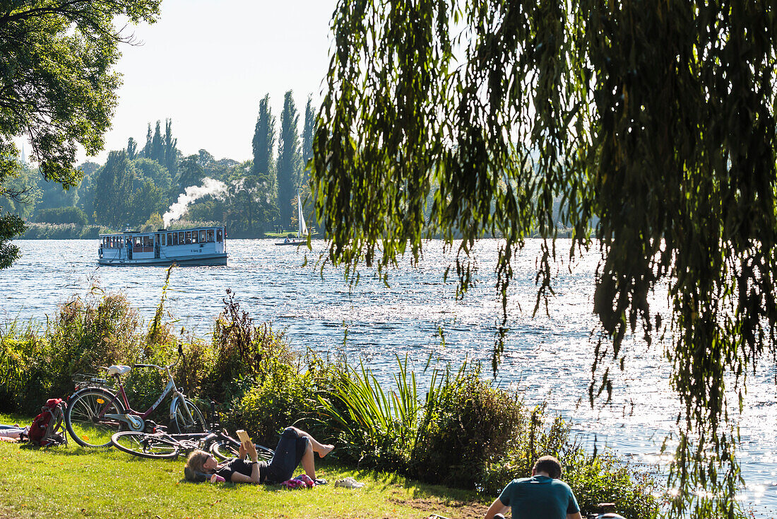 Ein historischer Ausflugsdampfer auf dem innerstädtischen See Außenalster passiert Leute die am Ufer ihre Freizeit genießen, Hamburg, Deutschland