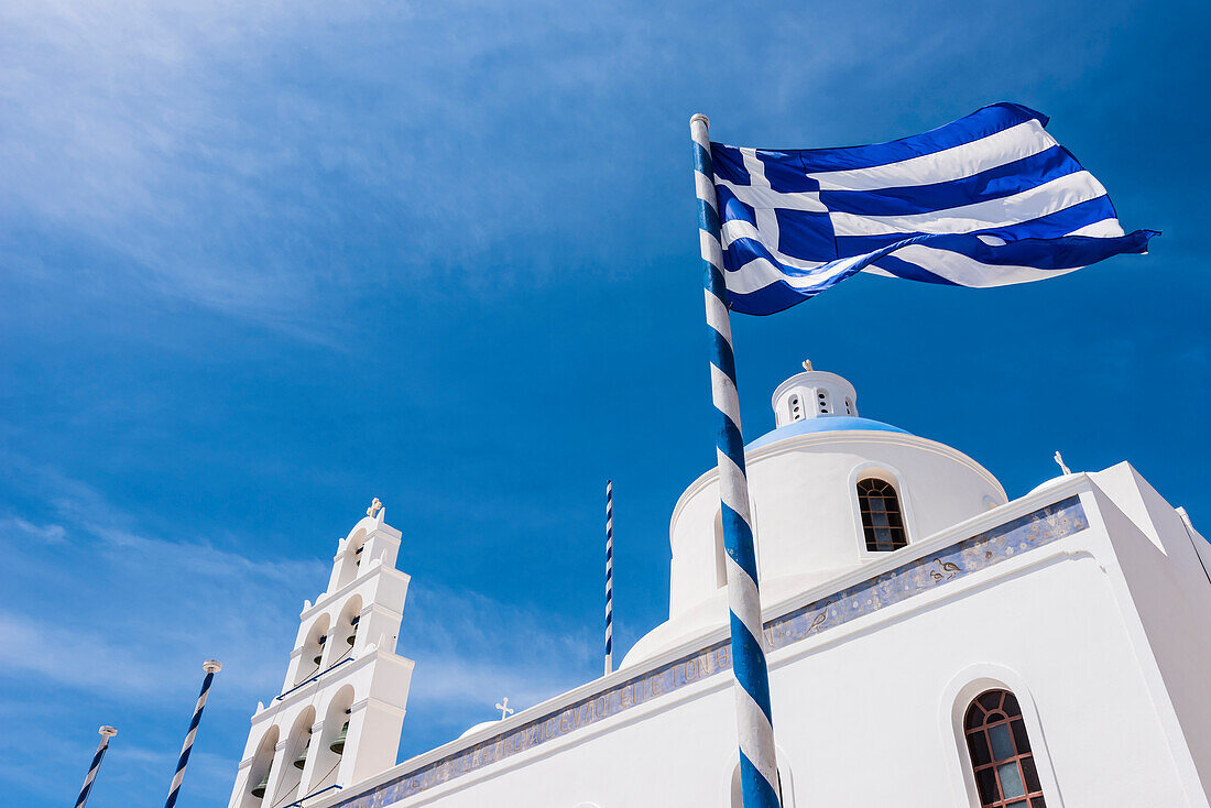 Glockenturm und Kuppel der im traditionellen weiß blauen Stil erbauten Kirche von Panagia Platsani auf dem Caldera Platz, mit der Nationalflagge, Oia, Kykladen, Santorini Griechenland