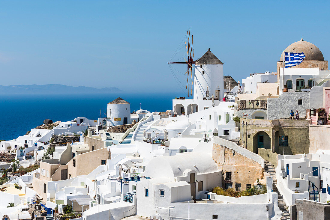 Blick auf die am Hang gelegenen traditionell gebauten weißen Häuser und die Windmühle, im Hintergrund das Mittelmeer mit der Nachbarinsel, Oia, Kykladen, Santorini, Griechenland