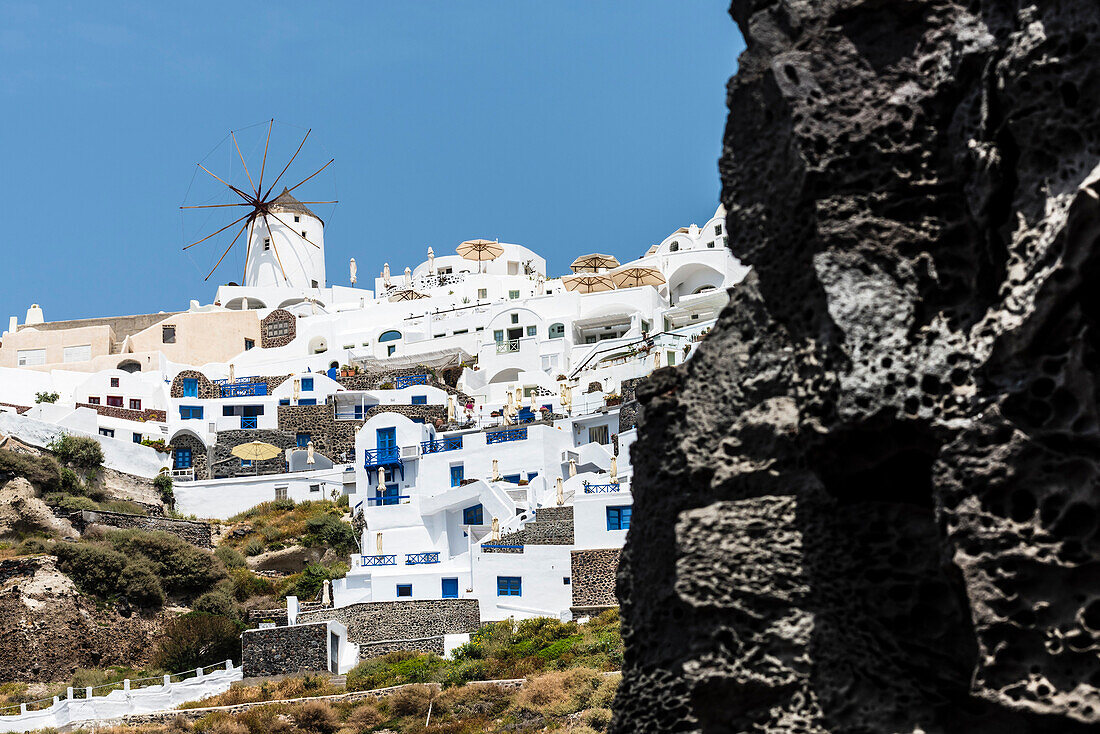 Blick auf die Steiküste und das Dorf mit der Windmühle und den traditionell gebauten Häusern, Oia, Kykladen, Santorini, Griechenland