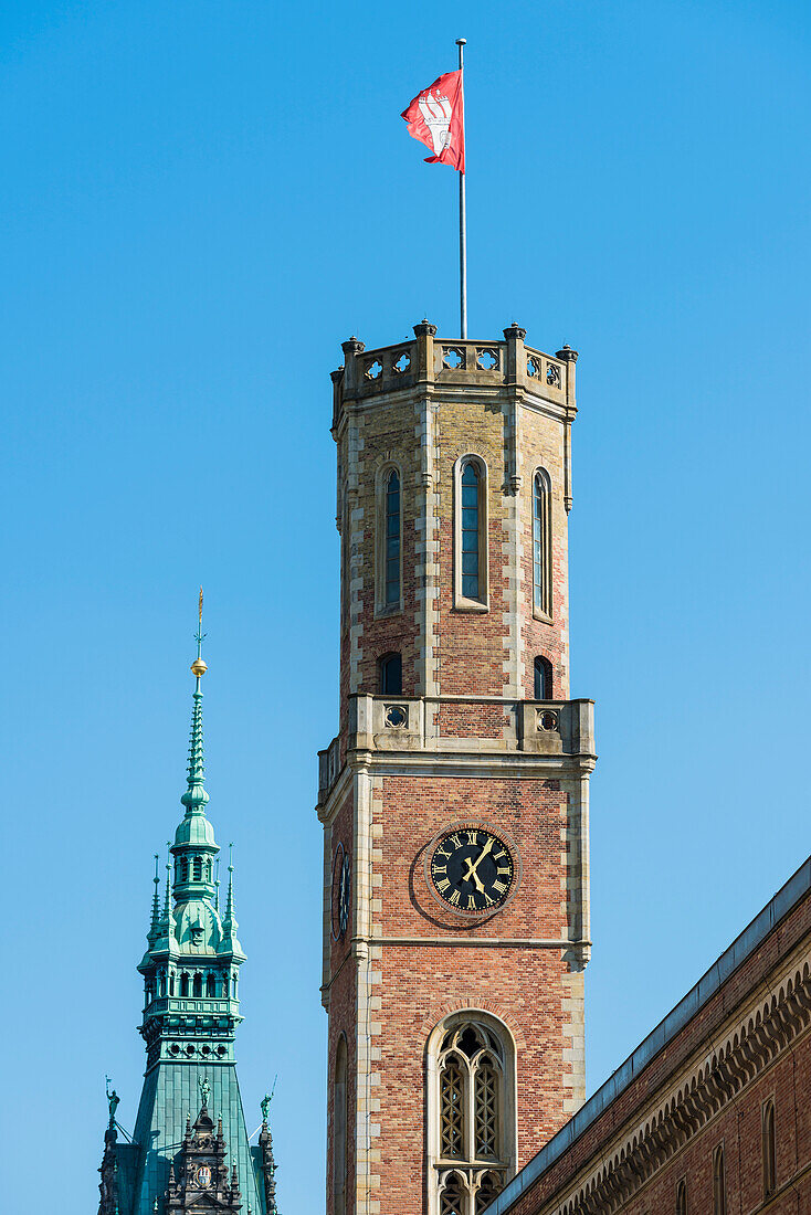 Tower of the Alte Post (former post office) with Hamburg flag and in the background the tower (112-m-high) in the historical style of the neorenaissance built city hall, Hamburg, Germany