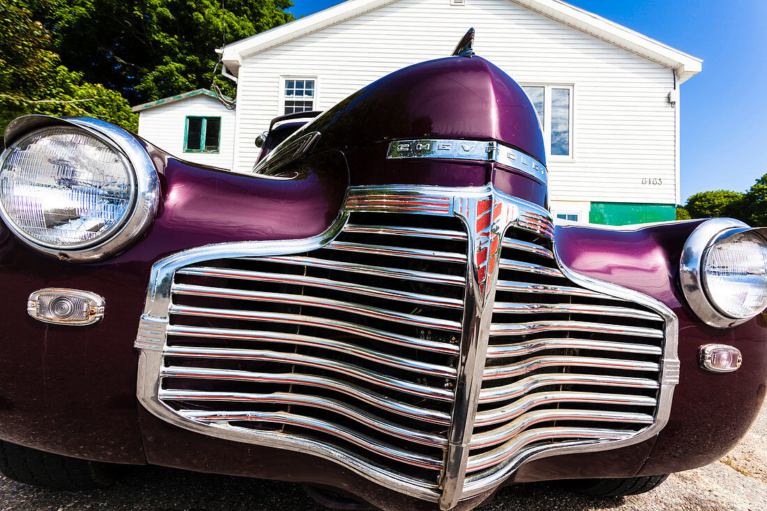 Der Kühlergrill eines alten Chevrolet vor einem typischen Holzwohnhaus auf dem Land, Digby, Nova Scotia, Kanada