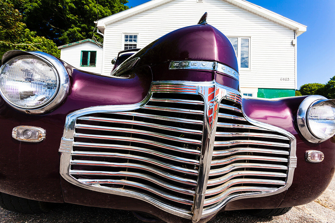 The radiator grill of a vintage Chevrolet in front a typical wooden residence building in the country, Digby, Nova Scotia, Canada