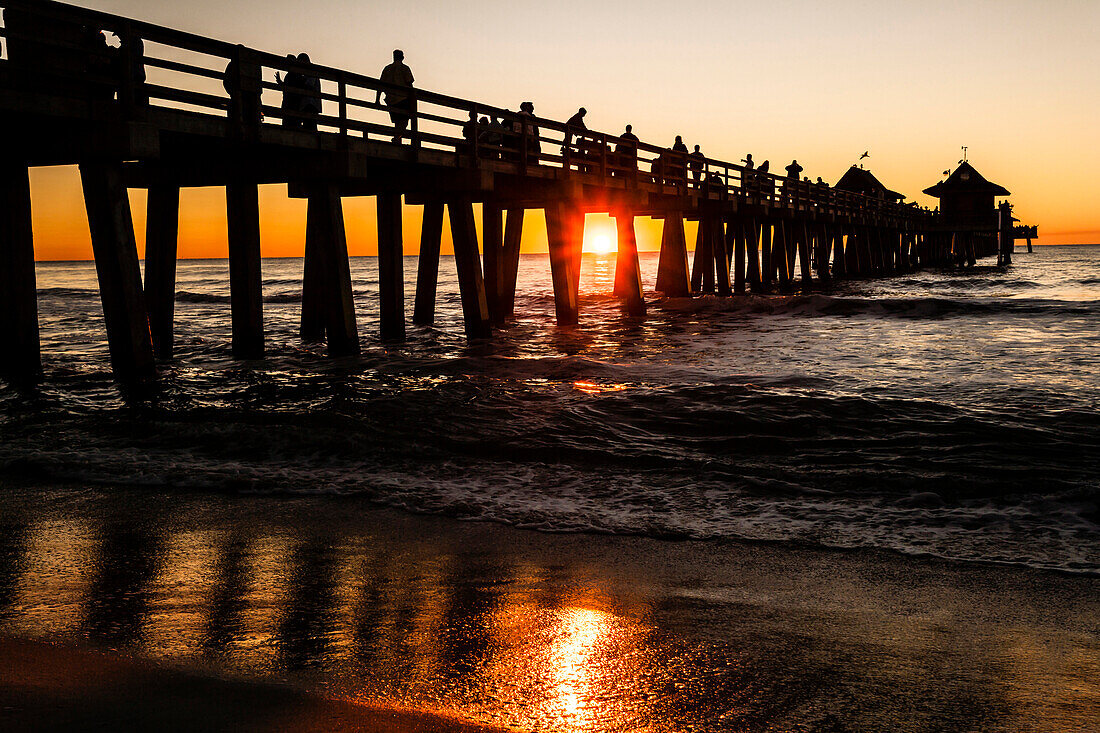 Pier aus Holz auf Stelzen am Golf vom Mexiko mit vielen Besuchern zum Sonnenuntergang, Naples, Florida, USA
