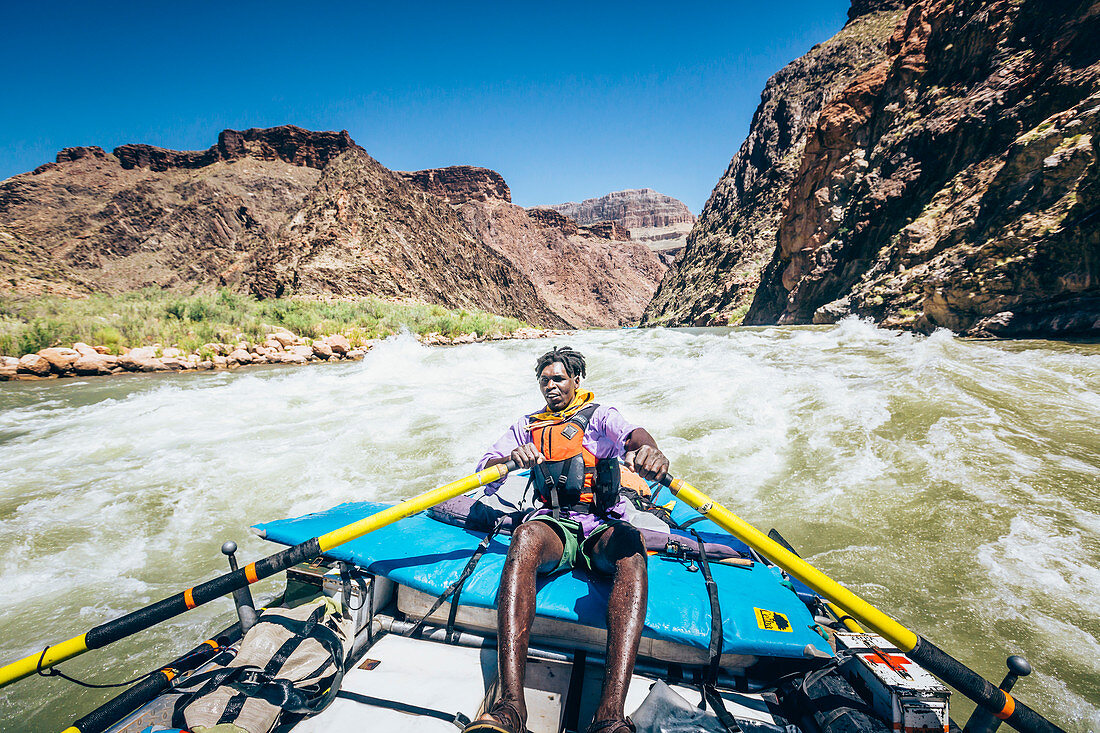 A man rows a raft through a rapid on the Colorado River, Grand Canyon National Park, Arizona, USA