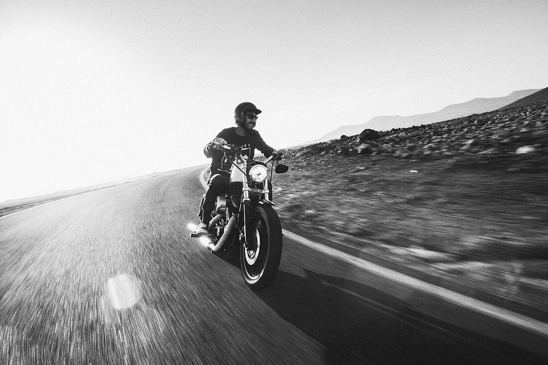 A man rides his Harley Davidson motor bike on an empty road in the desert just before sunset