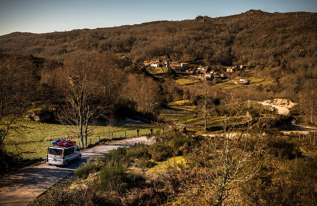A van with three whitewater kayaks drives down a scenic road in Portugal.