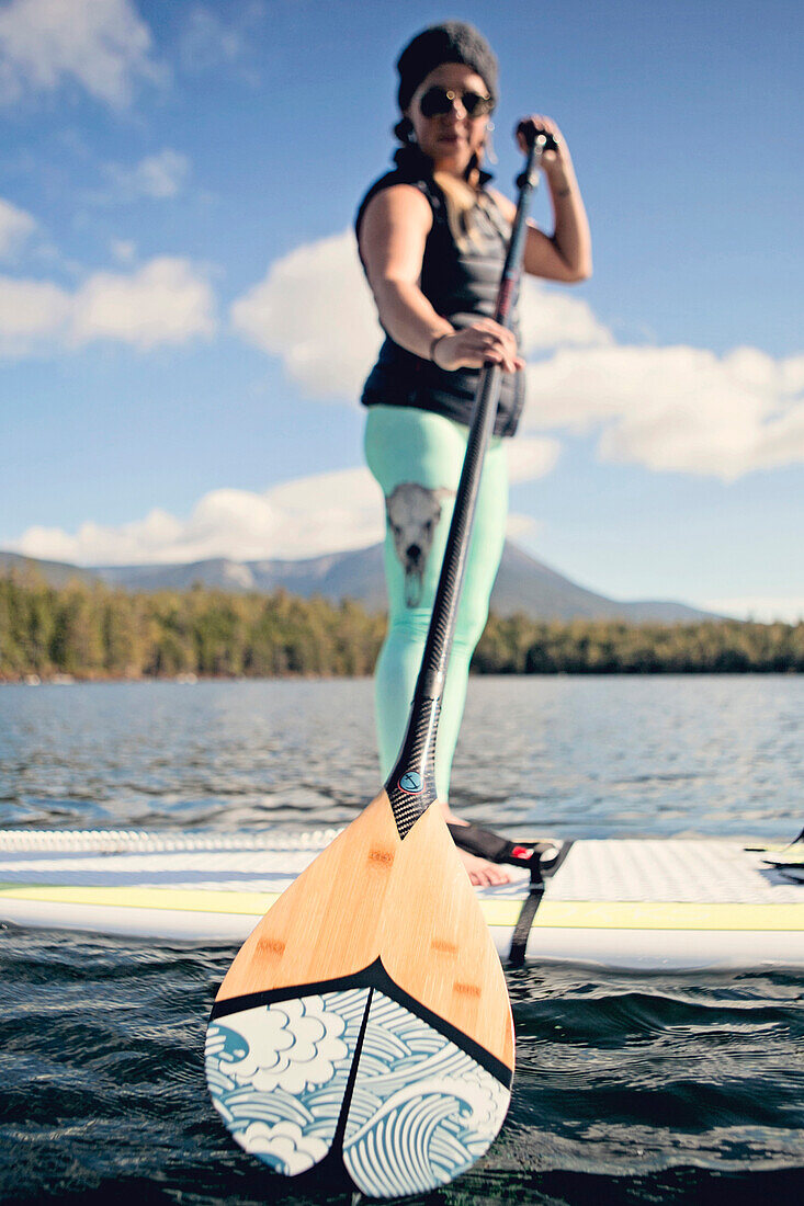 A young woman paddle boards on a pond in Maine.