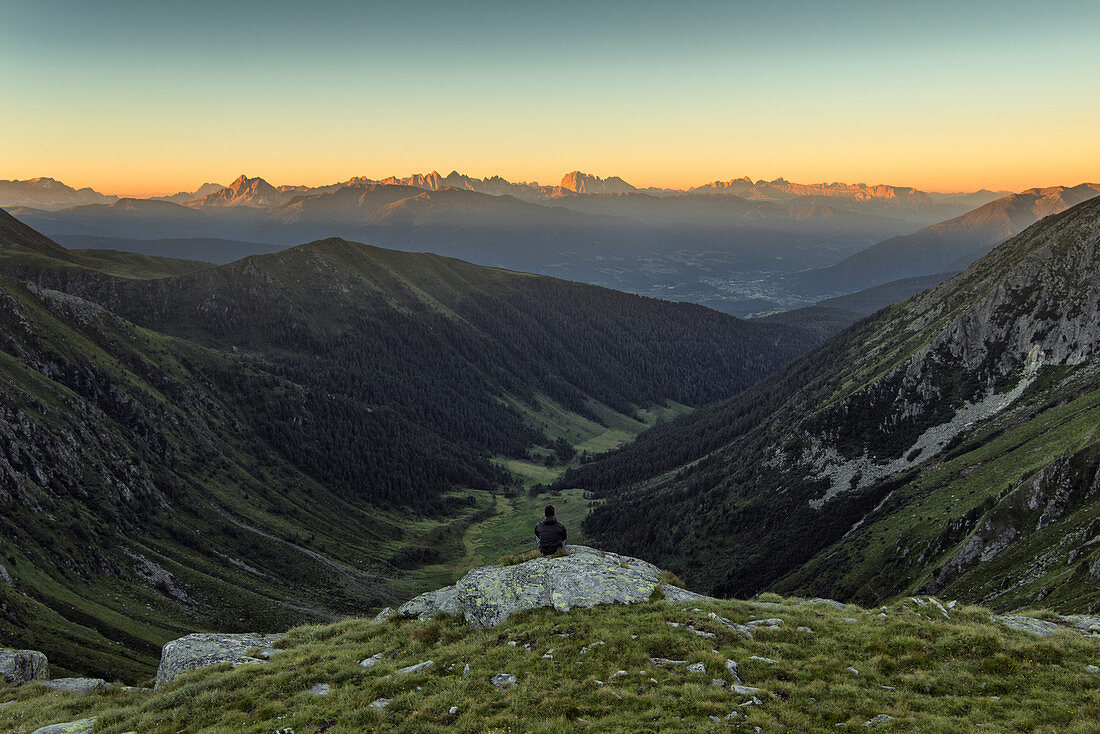 Hiker enjoying the morning view over Altfass Valley in Meransen, in the background the Dolomites, Unesco world heritage, in the first light of the day, South Tyrol, Italy