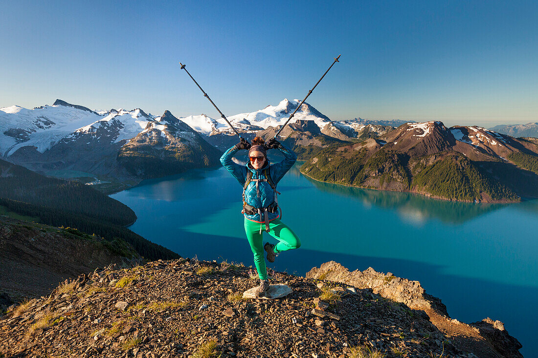 A backpacker makes a funny pose with her poles on the summit of Panorama Ridge in Garibaldi Provincial Park, British Columbia, Canada.