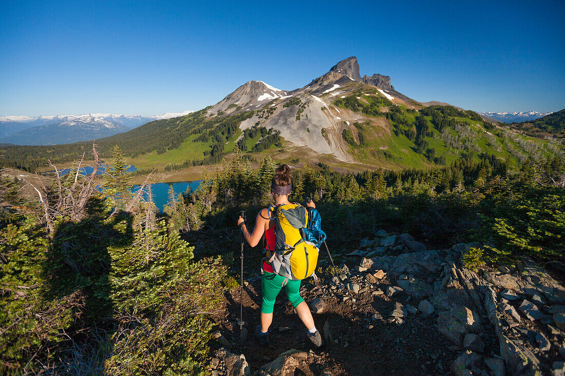 A photographer takes a picture of a young woman backpacking on the Panorama Ridge Trail with Black Tusk Mountain in the background in Garibaldi Provincial Park, British Columbia, Canada.